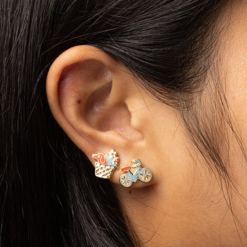 Mismatched bike and basket earrings featuring a bicycle design and a basket with a dog and flowers, in colorful enamel with gold-toned details.