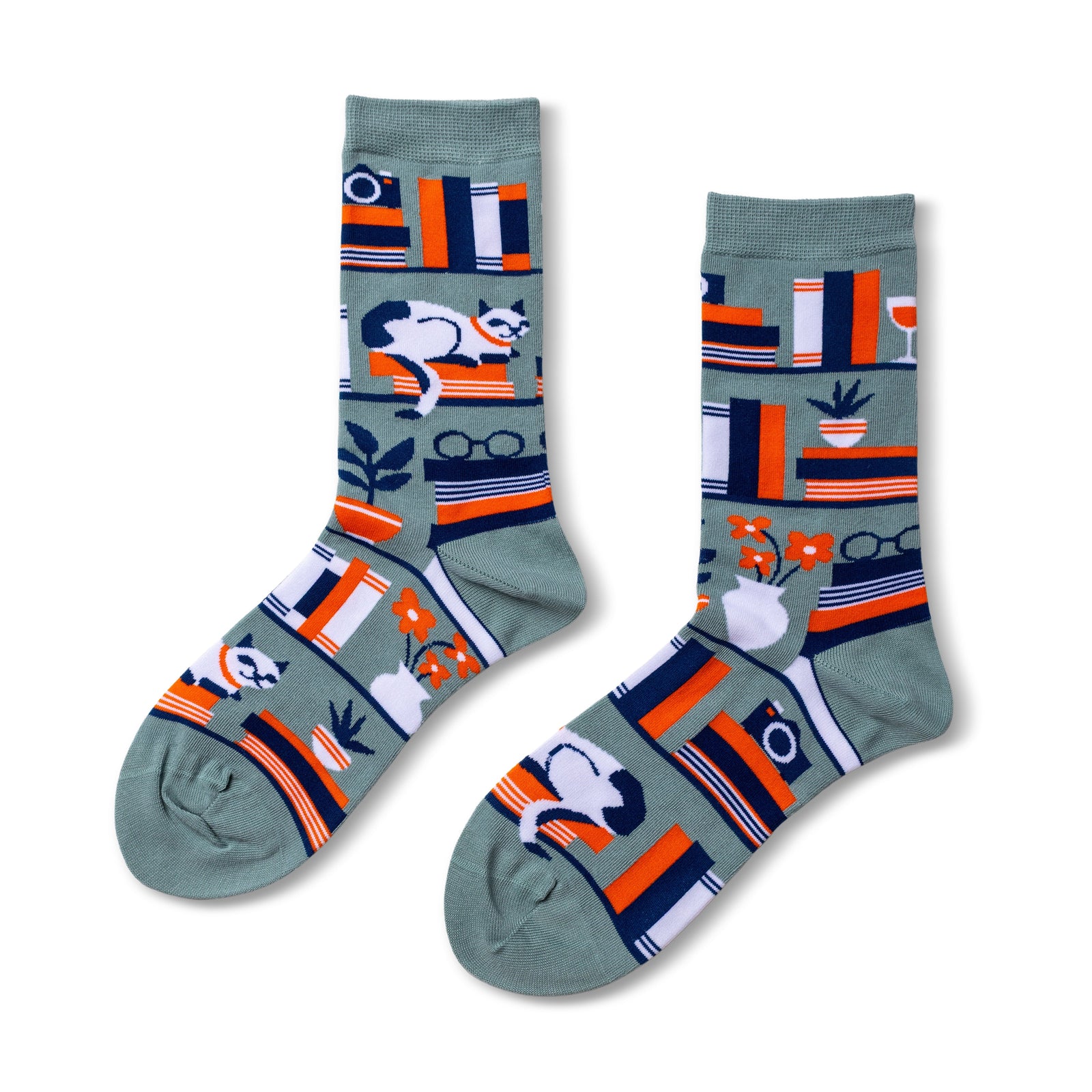 Sage green crew socks featuring illustrated bookshelves with books camera cat plant and reading glasses in orange navy and white by Yellow Owl Workshop
