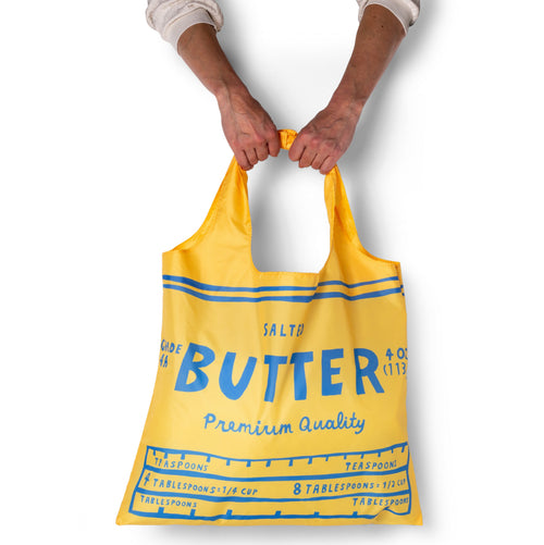 Person holding yellow illustrated butter tote bag with salted butter wrapper label design by Yellow Owl Workshop