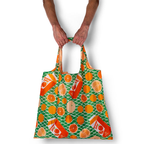 Person holding green illustrated citrus tote bag with orange fruit print by Yellow Owl Workshop