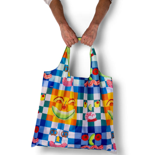 Person holding illustrated picnic tote bag with colorful playful food print by Kristina Micotti for Yellow Owl Workshop