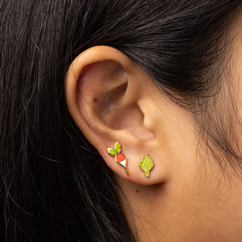 Close-up of an ear wearing a unique earring with a radish and artichoke design.