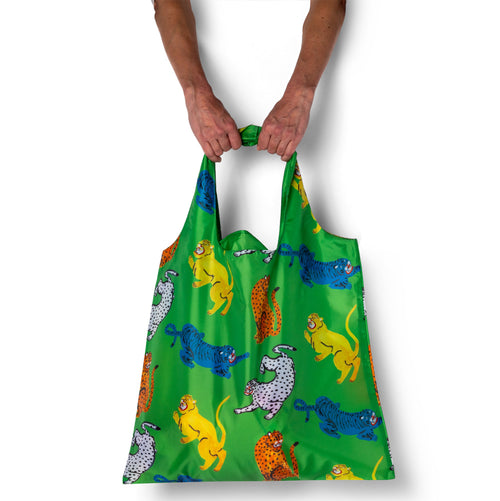 Alt text: Person holding green illustrated reusable tote bag with colorful wildcat print by Kristina Micotti for Yellow Owl Workshop
