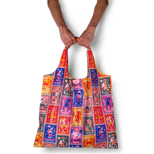 Person holding illustrated zodiac tote bag with colorful astrology symbols by Roisin O'Donnell for Yellow Owl Workshop