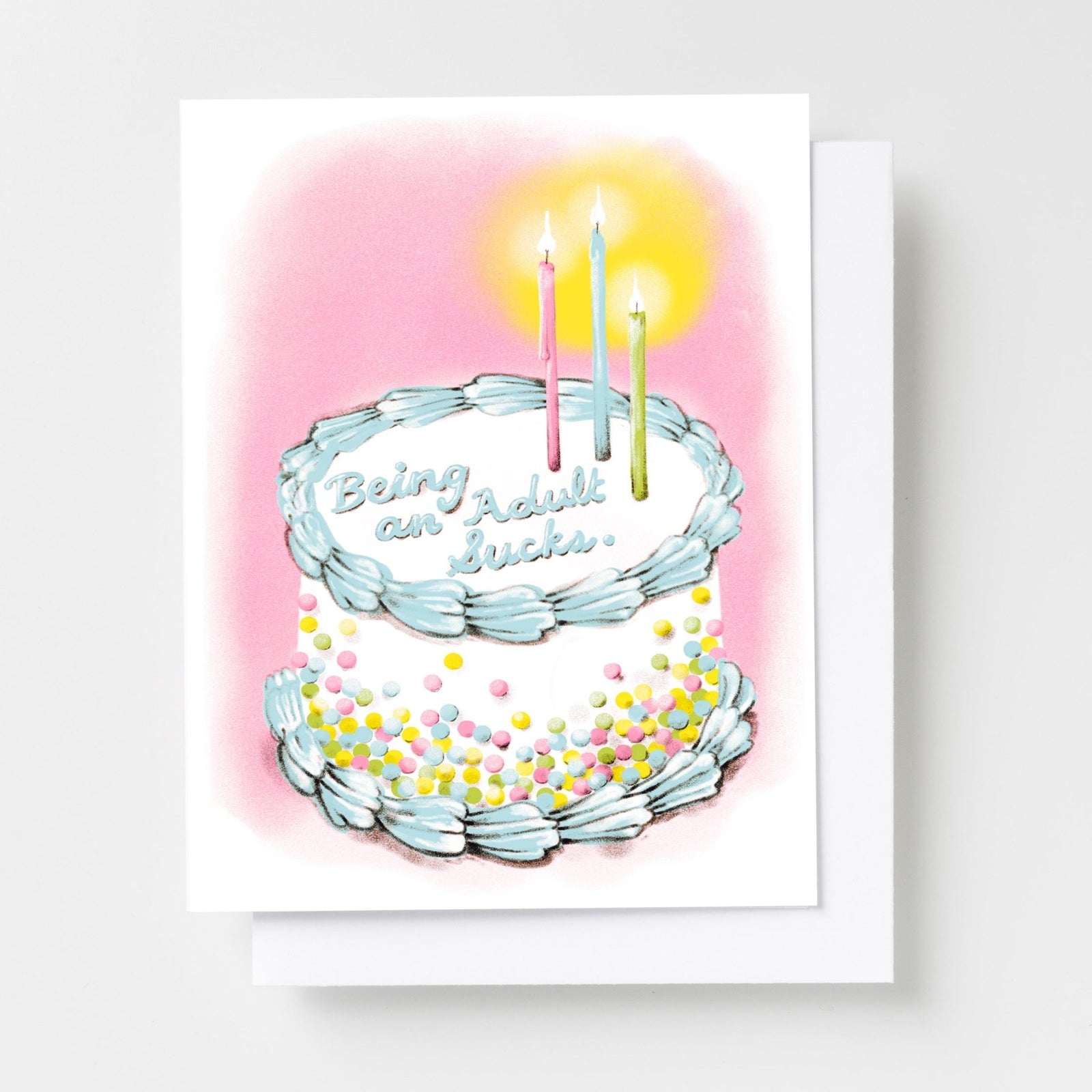 Risograph greeting card with an illustrated two-tier birthday cake with sprinkles and candles on a pink background, cake reads Being an Adult Sucks in cursive frosting lettering