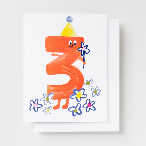 Risograph greeting card with an illustrated orange number three character wearing a party hat and holding a flower wand, surrounded by blue and pink flowers on a white background