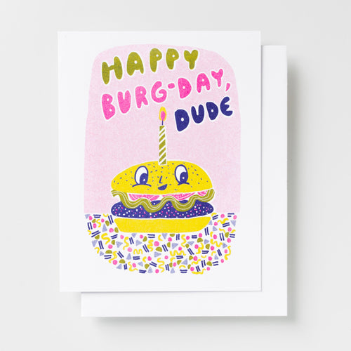 Risograph greeting card with an illustrated burger character wearing a birthday candle, text reads Happy Burg-Day Dude, in bold multicolor lettering on a pink background